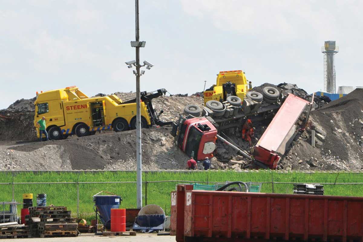 Vrachtwagen valt van puinberg bij afvalverwerker