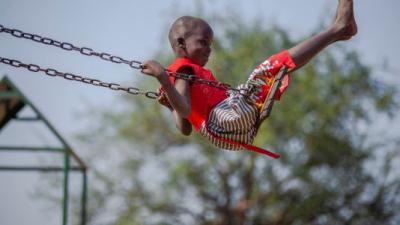 Een meisje schommelt buiten bij de kindvriendelijke ruimte in Palorinya Refugee Settlement in Obongi District, Oeganda