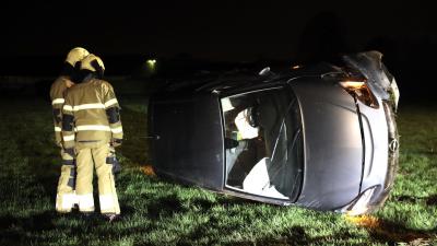 Auto op zijn kant in weiland